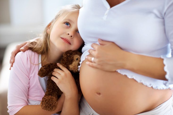 Sweet babby standing with her pregnant mother © Depositphotos