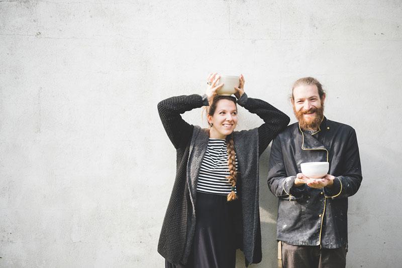 Couple standing in front of wall holding pots looking at camera smiling