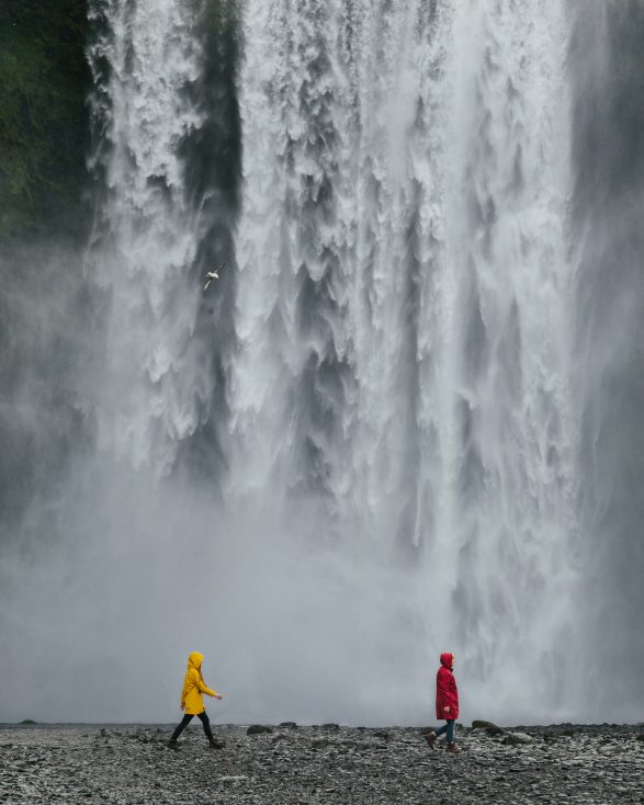 Couple of travelers in colored raincoats on the background of a large waterfall