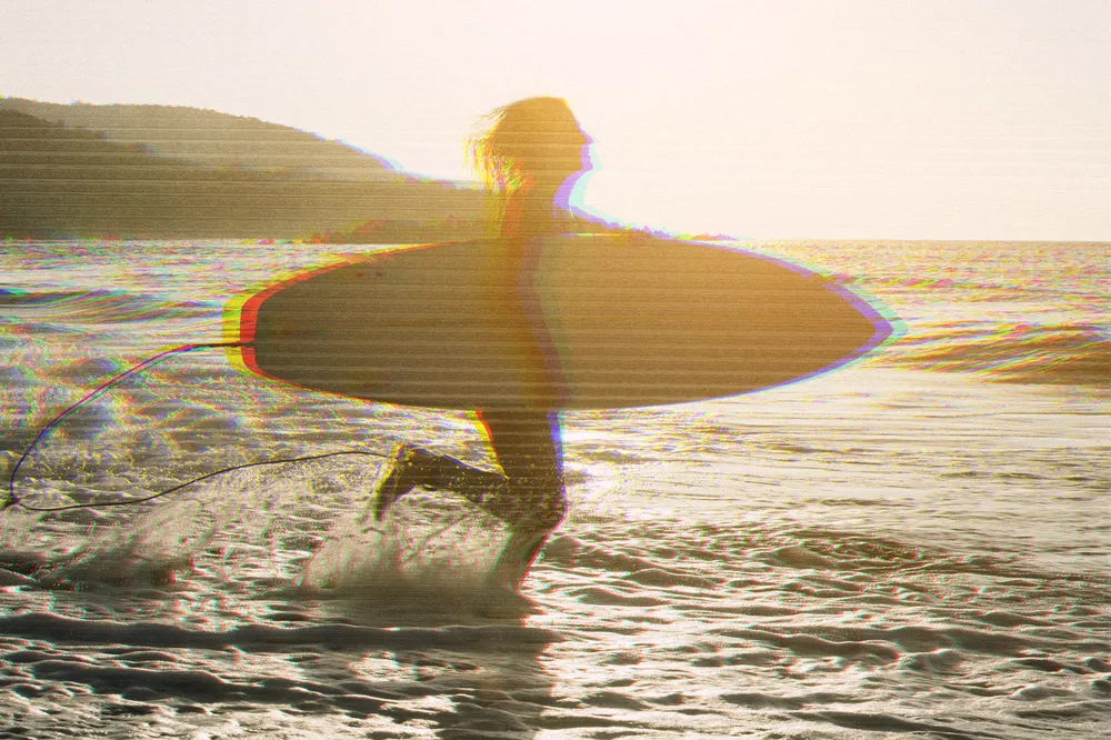 Woman with surfboard standing on wet sandy beach at the ocean.