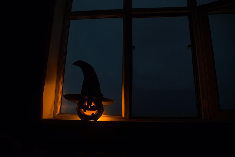 Scary Halloween pumpkin in the mystical house window at night or halloween pumpkin in night on room with blue window. Symbol of halloween in window.