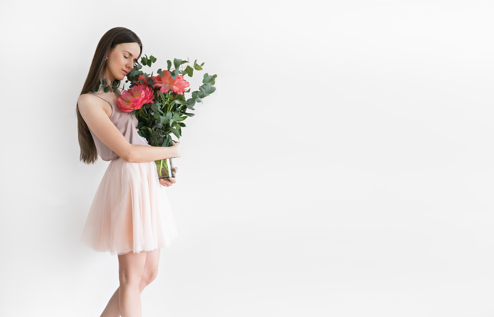 Beautiful girl with peonies in hands on a light background