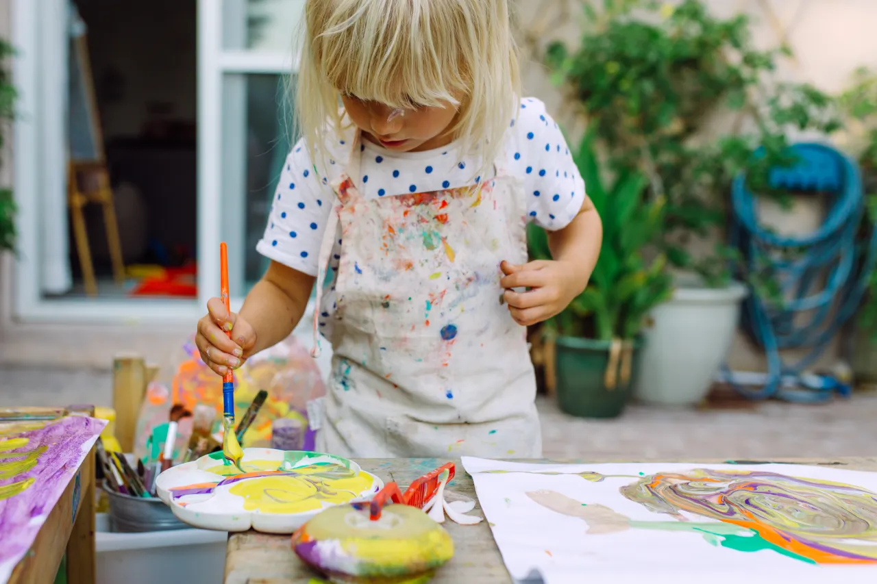 Little cute girl painting in the garden and mixing different colors