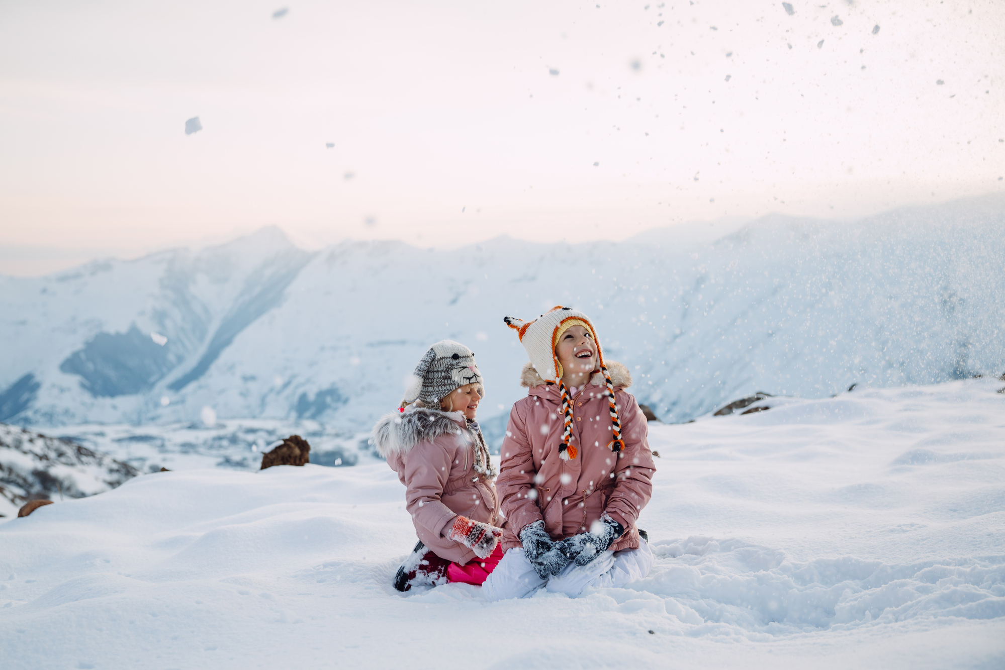 Two girls sitting in the snow and loooking at snowflakes falling