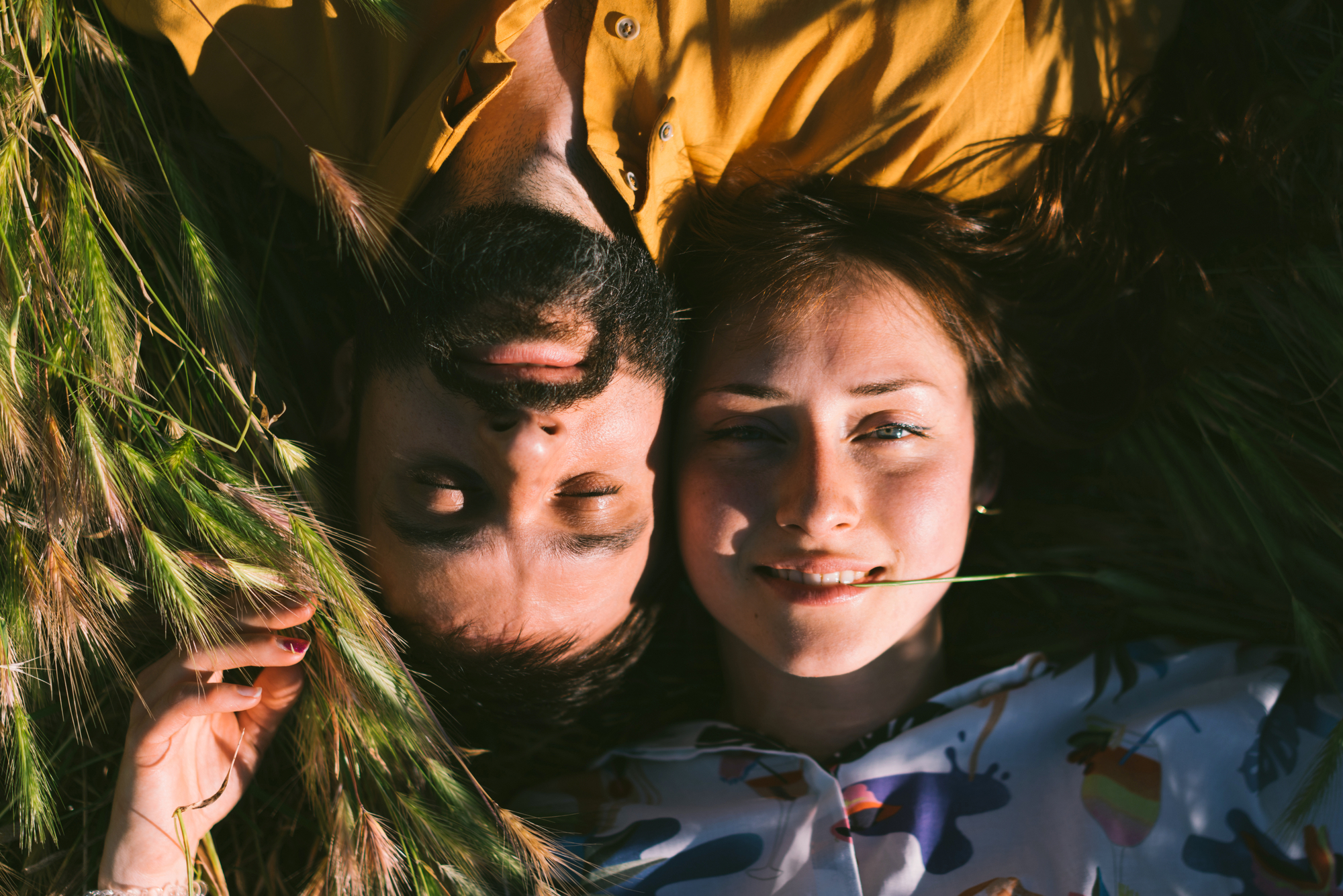 A romantic couple is enjoying warm sunny summer day while lying down amidst the meadow. A man and a woman in love are spending the weekend outdoors. Portrait of a young couple just married.