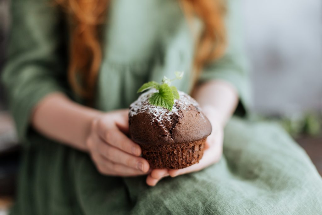 Nas mãos de um cupcake de chocolate decorado com uma folha verde