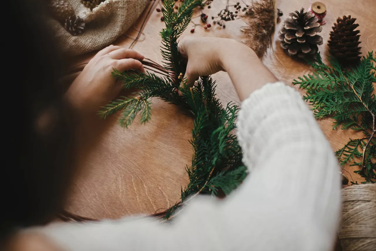 Girl hands holding fir branches and pine cones, thread, scissors