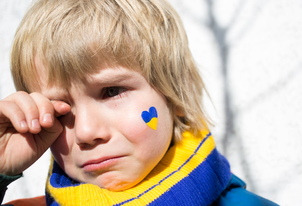 face of a frightened boy, a painted heart on the cheek in yellow-blue colors of the Ukrainian flag. Russia's invasion of Ukraine, a request for help to the world community. Children ask for peace