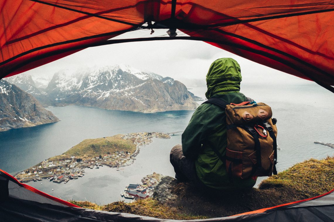 Man sitting on cliff edge alone enjoying aerial view backpacking lifestyle travel adventure outdoor summer vacations in Norway top of Reinebringen mountain