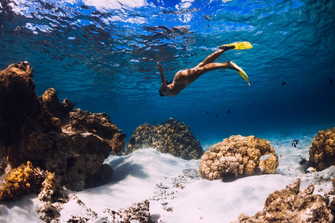 Woman freediver swimming over with yellow fins in blue ocean. Freediving or snorkeling in Mauritius