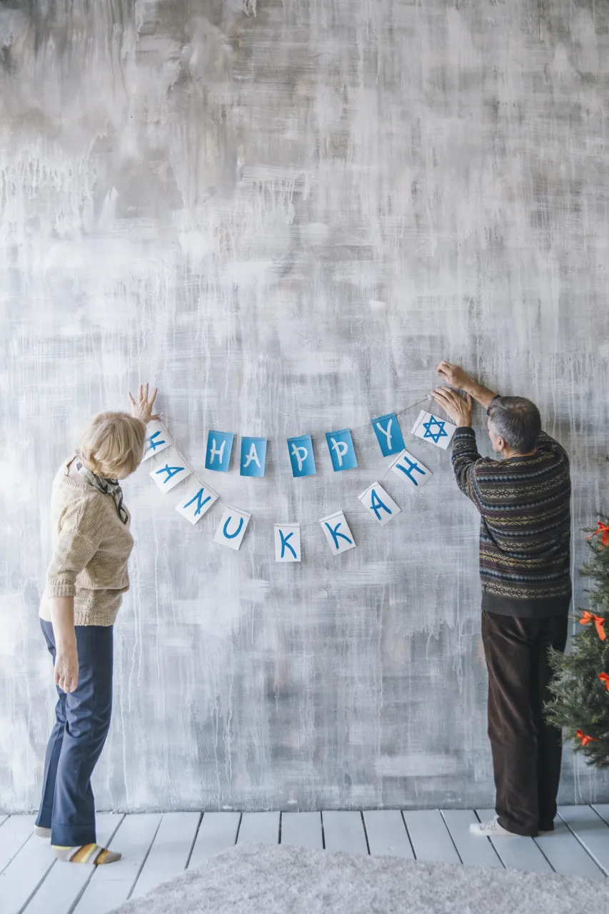 Two elderly people decorating the house with Christmas garlands