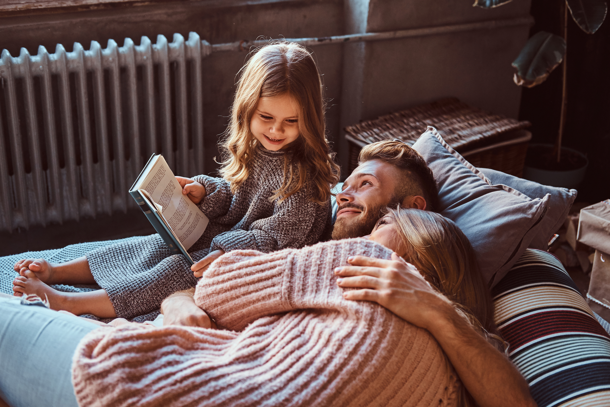 Mom, dad and daughter reading storybook together while lying on bed.