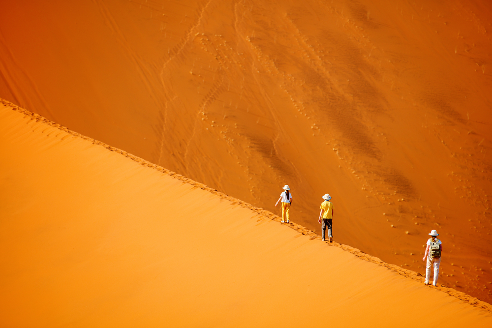 Family climbing up red sand dune