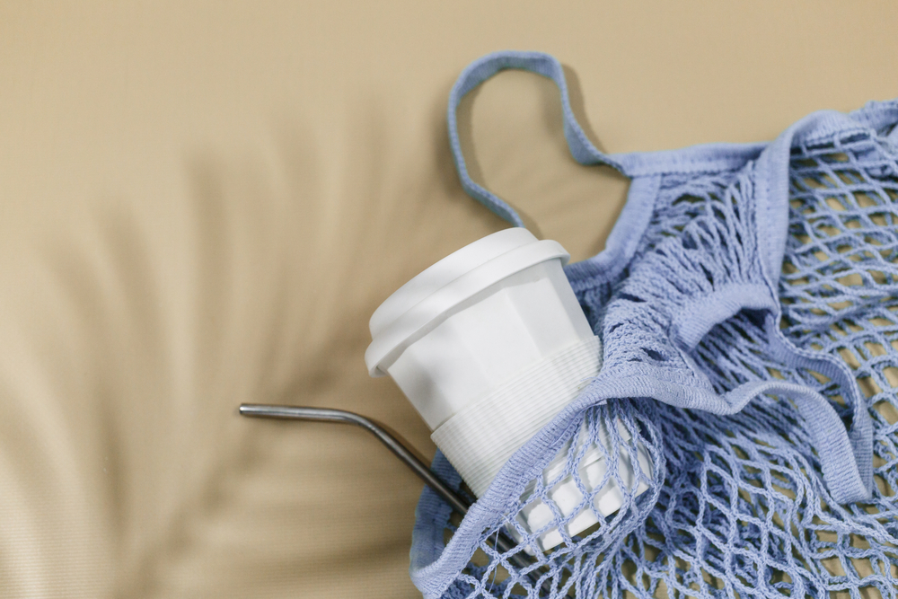 A reusable bag, a coffee mug and a straw on a beige background