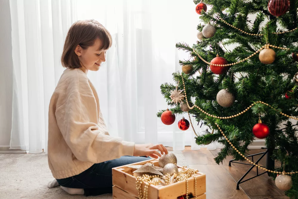 A teenage girl decorates a Christmas tree with a ball-shaped toy. Waiting and preparing for the holiday