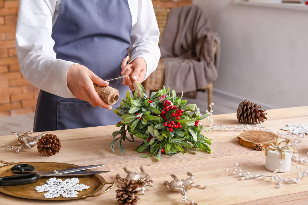 Woman making composition with mistletoe branches on table