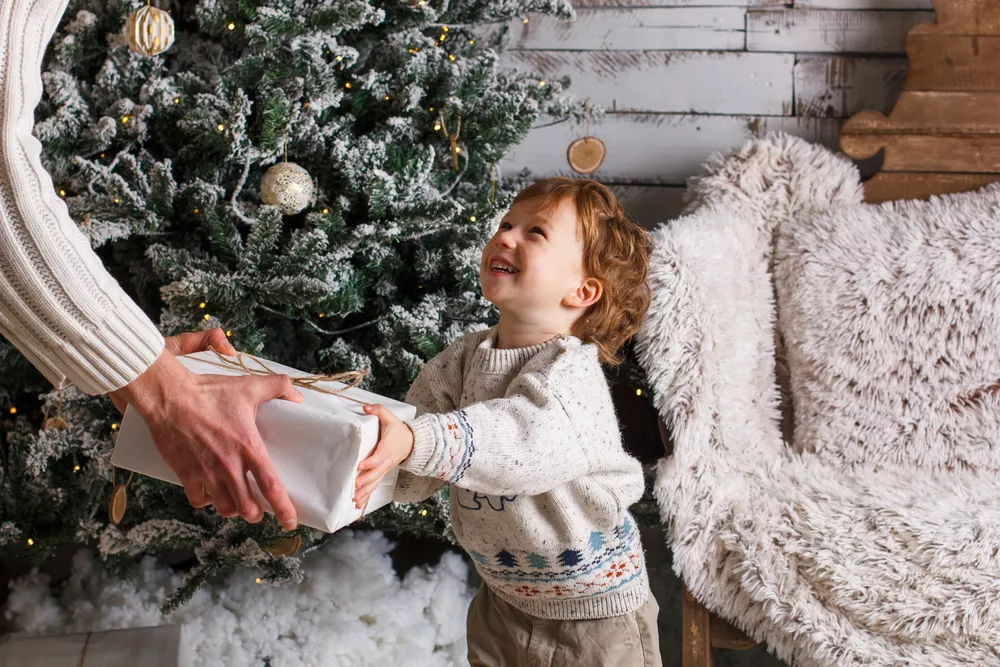 Happy father and son holding Christmas gifts in the living room. Chrismas tree and wooden background