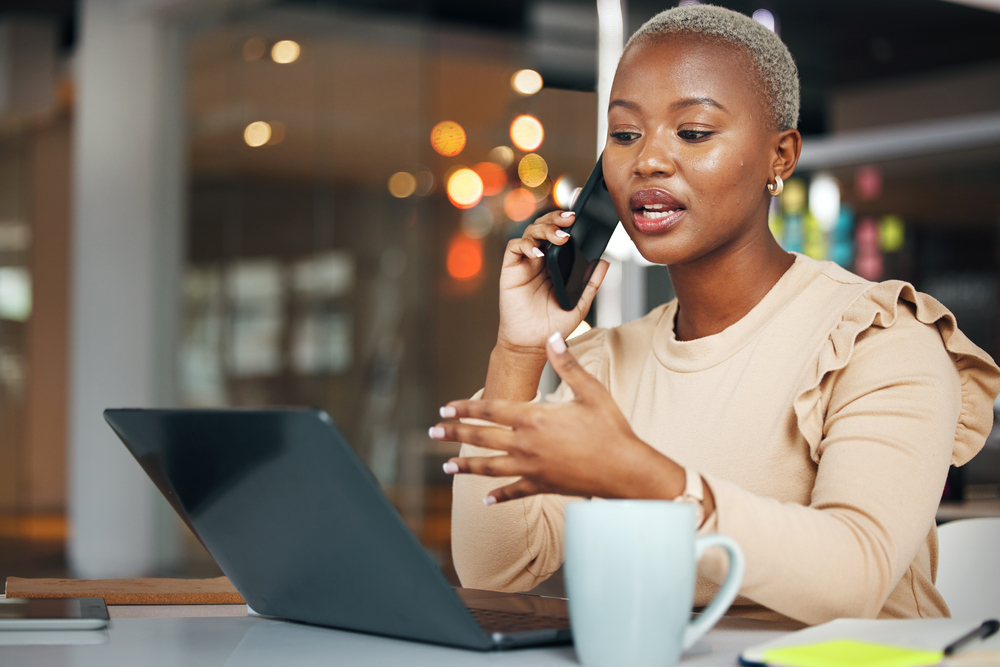 Photo phone call, business and black woman talking in office, chatting or speaking to contact. Laptop, cellphone and female professional in conversation, networking or discussion with smartphone at night