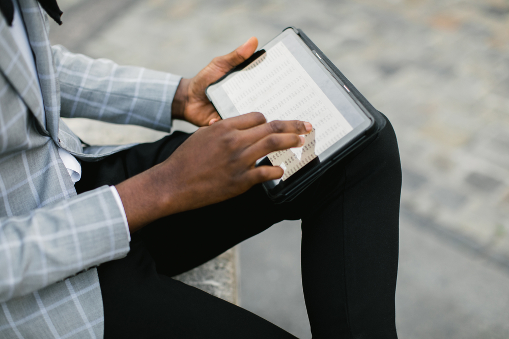 Close up of african man with digital tablet in hands sitting on city street. Focus on screen of modern gadget. People and technology concept.