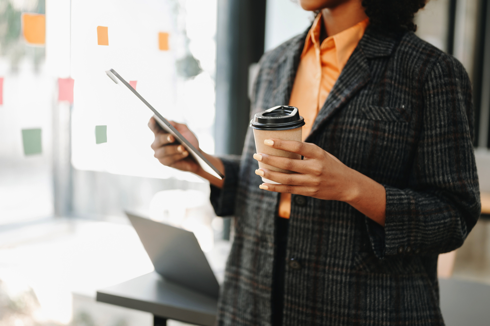 Photo confident beautiful businesswoman typing laptop computer and digital tablet while holding coffee at office