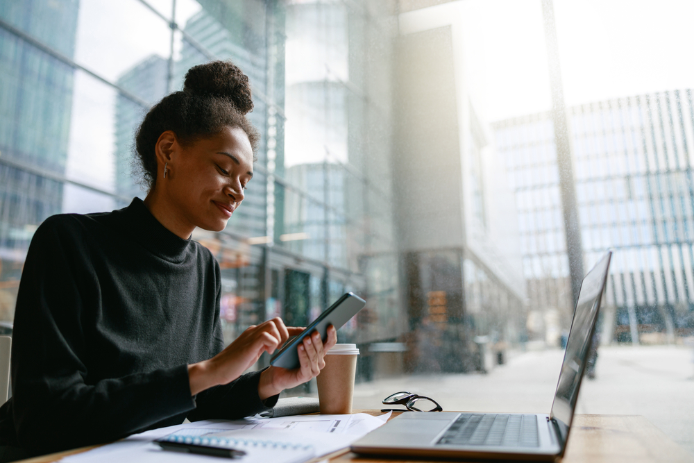 Photo smiling woman holding phone during working day in cafe sitting near window. Distance work concept