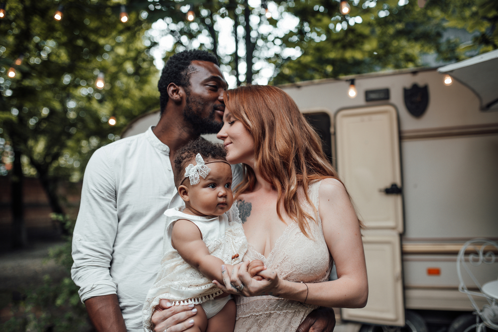 Outdoor portrait of loving couple holding little girl on hands. Family resting in park with trailer on background — Photo 