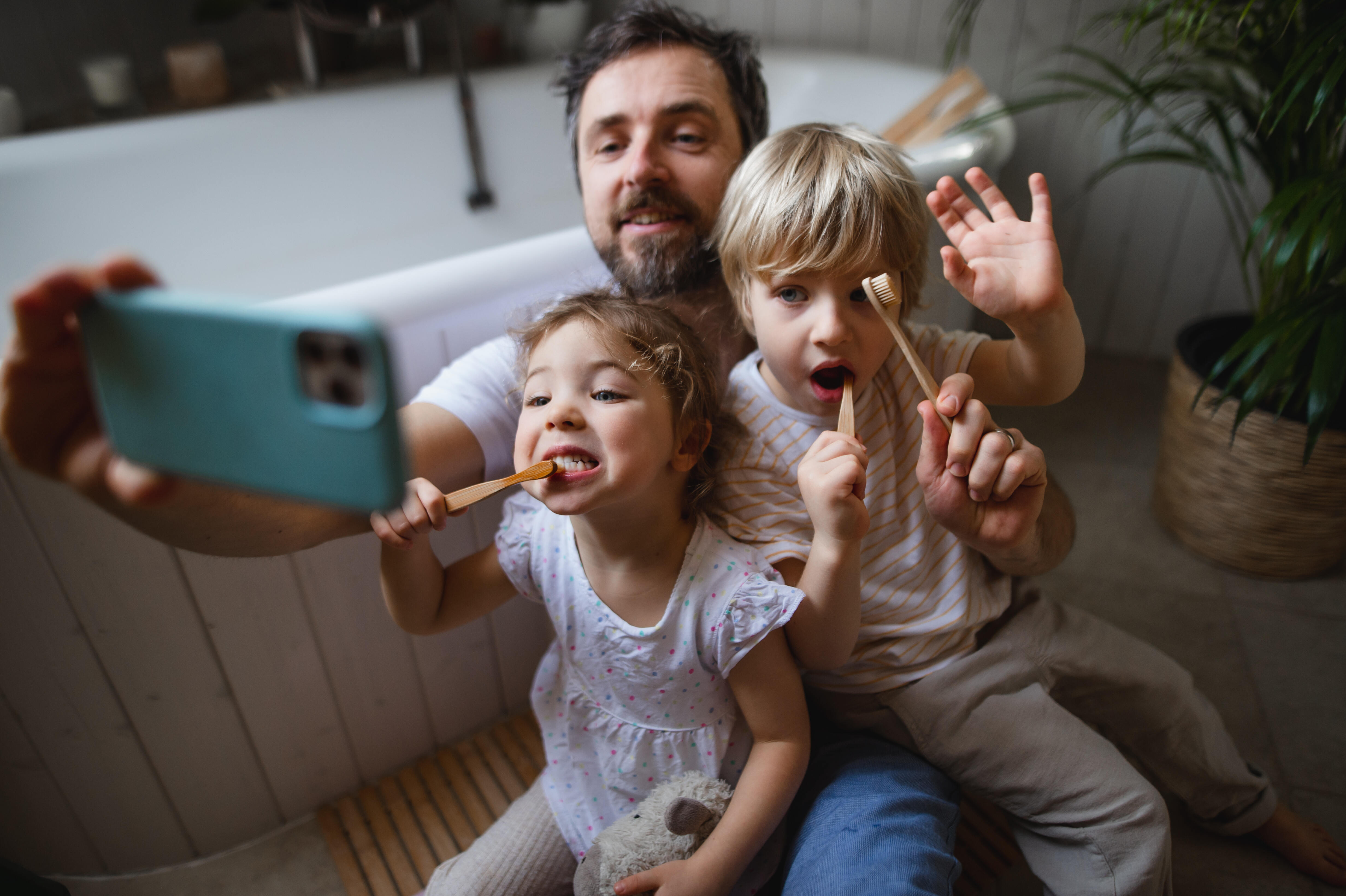 Photo mature father with two small children brushing teeth indoors at home, taking selfie.