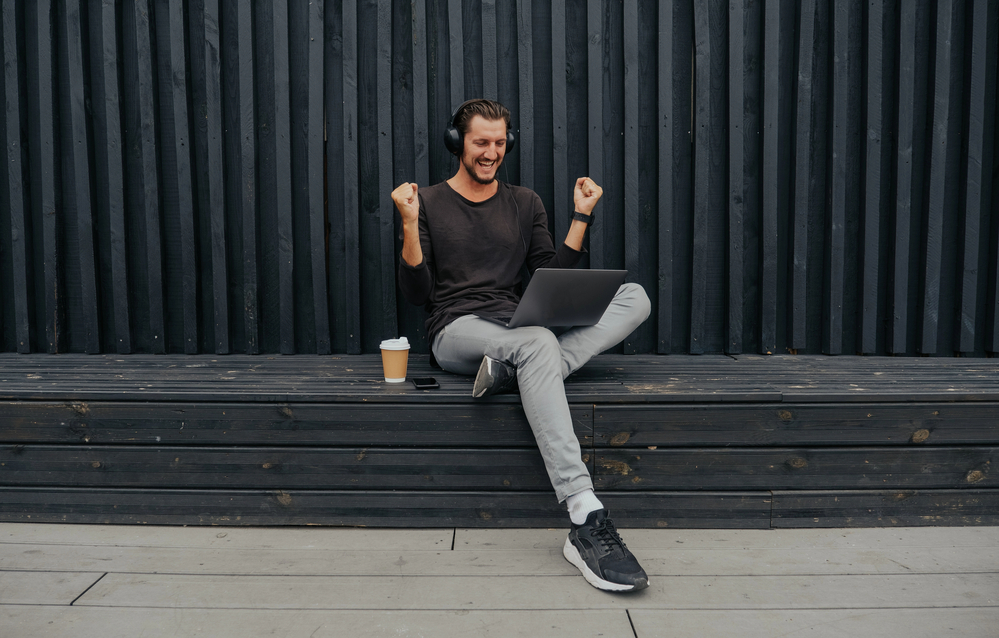 Photo Freelancer Man siting in urban city with a laptop phone camera and coffee or tea with misic headphones