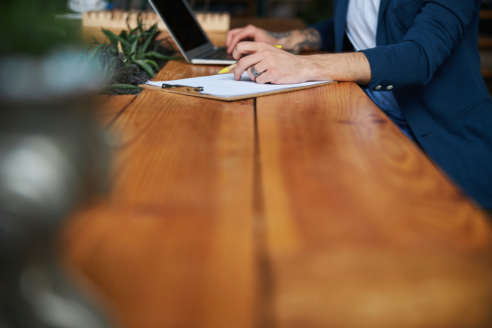 Photo Close up of young man with pen in his hand sitting at the table and working on modern notebook