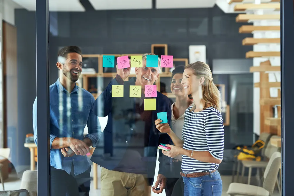 Group, people and sticky notes on glass for project ideas, planning and schedule management of startup. Staff, teamwork and paper for brainstorming, support goals or productivity solution in office.