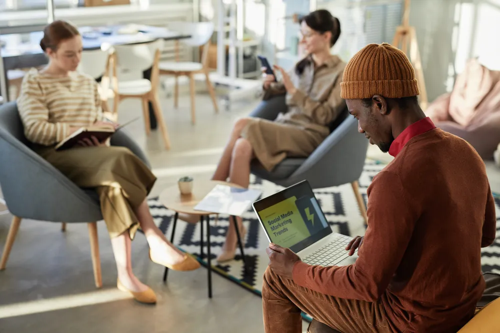 Side view portrait of young black man typing at laptop with marketing statistics on screen in company office, copy space