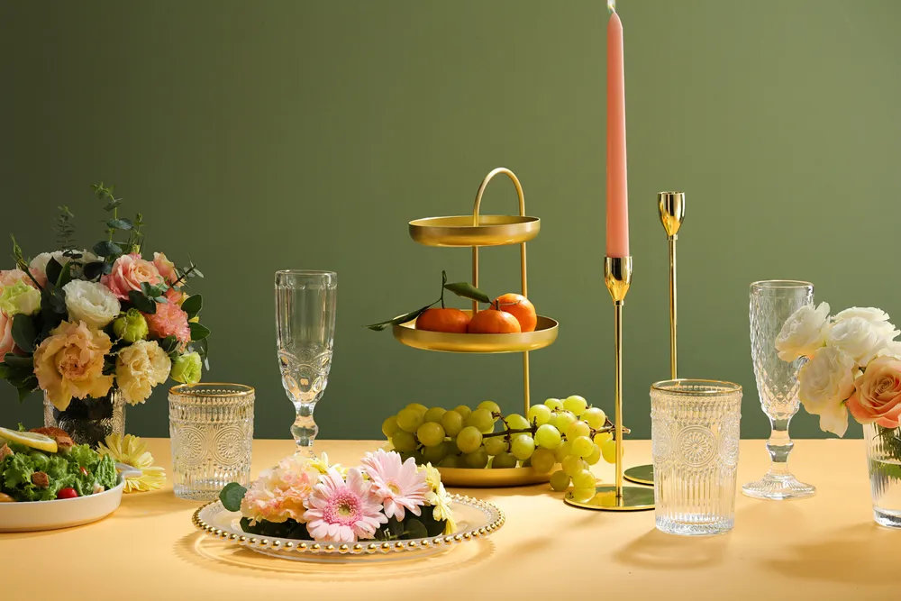 Wedding table setting with white plates and glass decorated with candles, green leaves, flower, tiered tray with fruit.