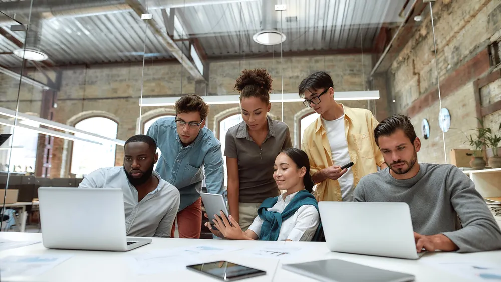 Successful multicultural team. Young business people in casual wear using modern technologies and working together on new project while sitting in the creative office. Team building concept.