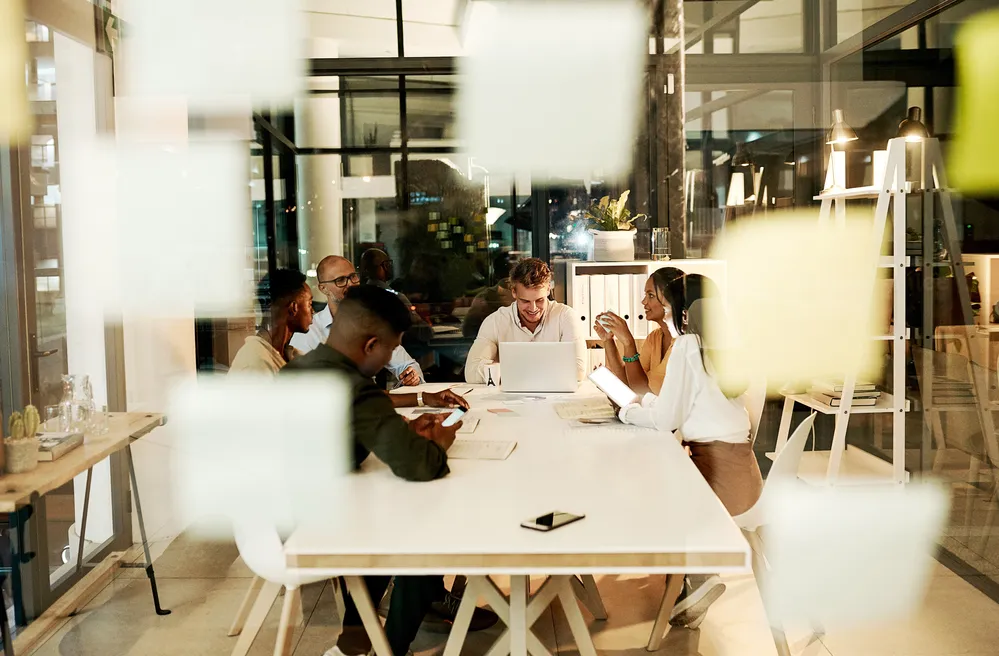 Professional, creative and casual business people in meeting with laptop, talking and planning a project together in an office at work. Diverse, happy and smiling team of workers discussing strategy