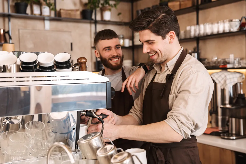 Group of cheerful men baristas wearing aprons working at the counter in cafe indoors, talking