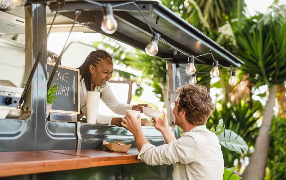 Afro food truck owner serving meal to male customer - Modern business and take away concept