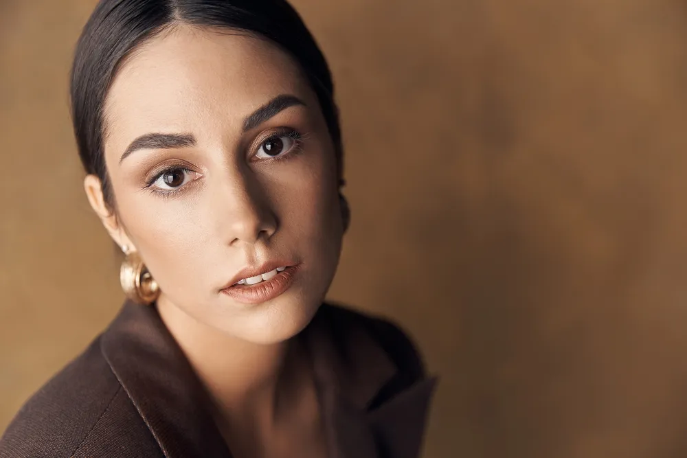 portrait photo of a beautiful stylish girl in a brown suit,on brown background in studio, she mysteriously looks into the camera with her brown eyes