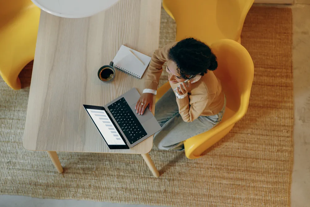 Top view of female freelancer is talking phone working on laptop from home. Distance work concept