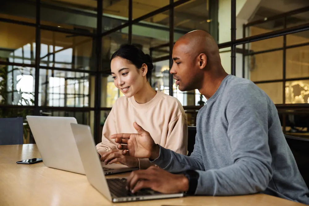 Image of multiethnic young female and male coworkers sitting at table and working on laptops in office — Photo 