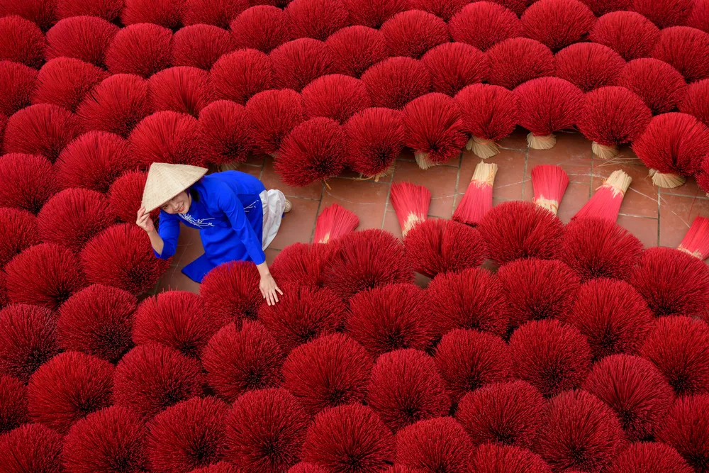 Asian woman in a traditional ao dai dress working for drying bundles of Incense sticks at Hanoi, Vietnam.